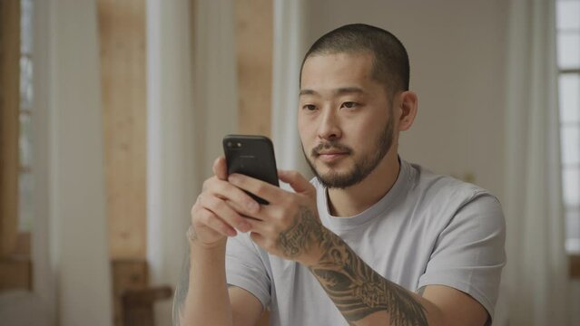 Close up of an asian tattooed man winning and achieving something on his smart phone