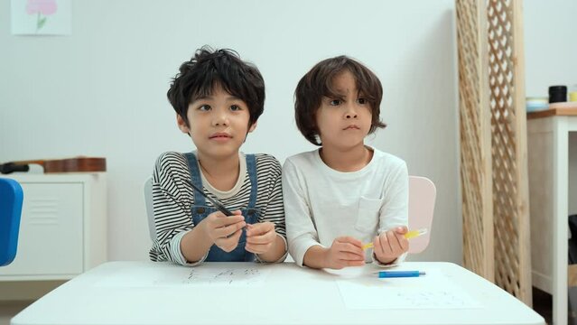 Happy asian two boy kids creatively draw and talk with brushes and crayon on the table. Little boy kindergarten preschool student in class.First time to school education,Childhood education concept.