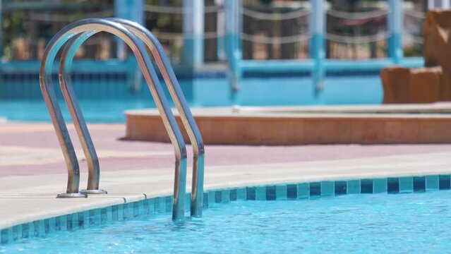 Close up of swimming pool stainless steel handrail descending into tortoise clear pool water. Accessibility of recreational activities concept