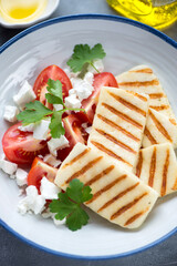 Slices of grilled halloumi cheese with red tomatoes, feta cheese and fresh parsley, close-up, vertical shot, selective focus