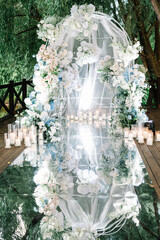 Arch design for the wedding ceremony is decorated with flower arrangements and stands on the park background. modern transparent chairs for guests 