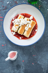 Plate of pan fried georgian crepes with cottage cheese stuffing and strawberry sauce, above view on a blue stone background with space