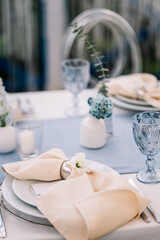 Outdoor banquet and modern design for wedding ceremony in summer. Linen tablecloth, candles, flowers and accessories, glasses and plates on table for guests with chairs, flat lay, nobody