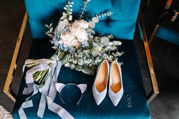 Bridal bouquet. Bridal shoes. Rings. The bride's bouquet. Beautiful bouquet of white, blue, pink flowers and greenery, decorated with long silk ribbon lies on a blue chair