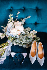 Bridal bouquet. Bridal shoes. Rings. The bride's bouquet. Beautiful bouquet of white, blue, pink flowers and greenery, decorated with long silk ribbon lies on a blue chair