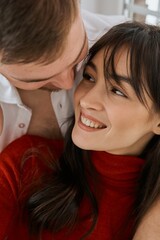 A loving couple sits near the window in an embrace. A girl in a red dress with her beloved boyfriend. Engagement..