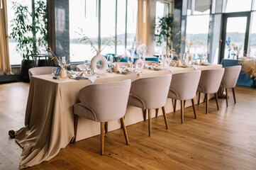 Long dinner tables covered with white cloth, served with porcelain and blue glasses and rich decorated with flowers 