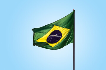 Uma bandeira do Brasil balançando ao vento com céu ao fundo.