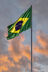 Uma bandeira do Brasil balançando ao vento com céu ao fundo.