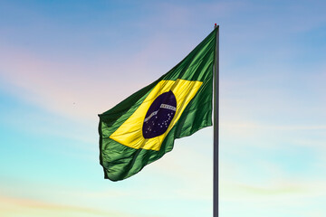 Uma bandeira do Brasil balançando ao vento com céu ao fundo. - obrazy, fototapety, plakaty
