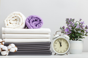 Stack of bed linen, bed sheets and towels with cotton branch and potted plant alarm clock on table