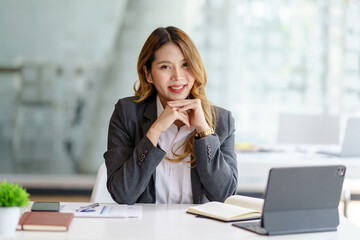 Confident successful Asian business woman sitting smiling looking at camera in office.