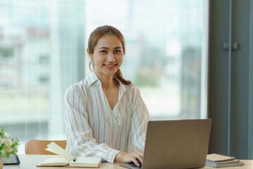 Confident successful Asian business woman sitting smiling looking at camera in office.