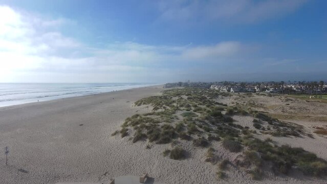 aerial footage of gorgeous silky brown sand dunes along the beach covered with lush green plants and grass with vast blue ocean water and people on the beach at Oxnard State Beach Park in Oxnard