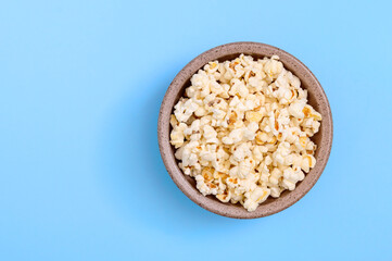 Bowl of tasty popcorn on a blue background. Top view with copy space.