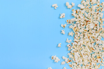 Tasty salted popcorn scattered on blue background with copy space. Cinema, movies and entertainment concept.