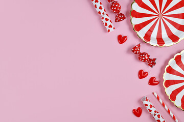 Obraz premium Party flat lay with red paper plates, heart ornaments, candy and drinking straws on pink background with copy space