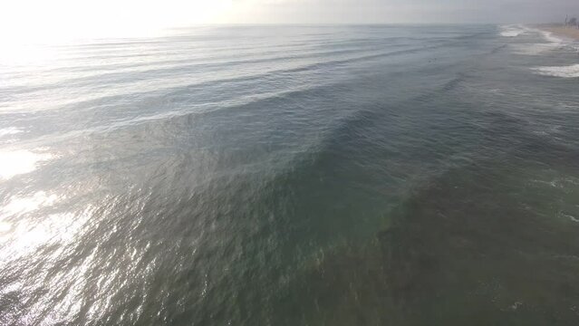 aerial footage of the rippling vast blue ocean water with majestic waves braking and rolling into the beach at Oxnard State Beach Park in Oxnard California USA