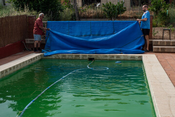 Destapando la piscina al inicio del verano dos hombres, agua sucia y verde, necesidad de...