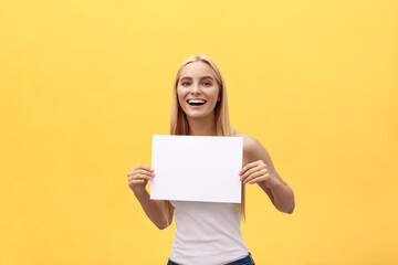 Obraz na płótnie Canvas young beautiful girl smiling and holding a blank sheet of paper, isolated on pastel yellow background.