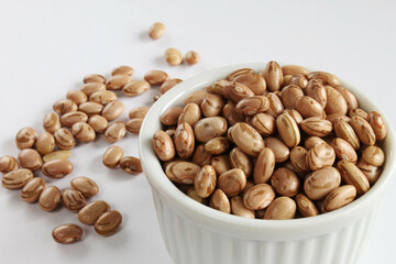 Pinto beans bowl with grains scattered on the white background.