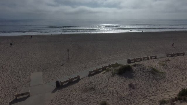 aerial footage of a gorgeous sunset over the vast blue ocean water with majestic waves rolling into the beach with people walking in the sand at Oxnard State Beach Park in Oxnard California USA