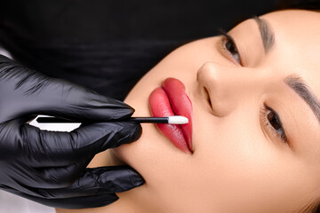 work after permanent make-up, the master smoothes lips with a cotton swab, moisturizing them with...
