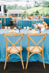 Cozy outdoor Wedding. Banquet. Chairs and honeymooners table decorated with candles, served with cutlery and crockery and covered with a blue tablecloth. 