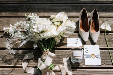Wedding details. On the woodden floor are an envelope, an invitation, wedding rings and a bouquet of flowers and candle as a gift for guests