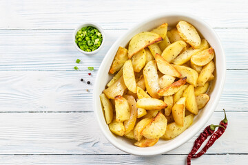 Seasoned baked potato wedges in baking dish on wooden background. Top view, copy space.