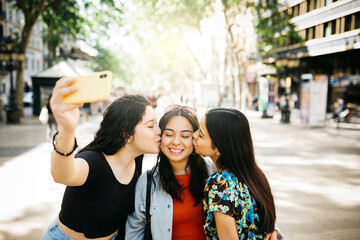 Three young women walking down Las Ramblas of Barcelona and taking a selfie, while kissing, with a phone