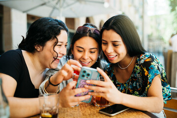 Three young women looking at a phone on terrace of a restaurant