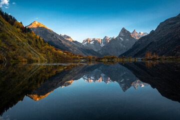 Mountain reflection on the lake. Beautiful landscape with high mountains with illuminated peaks and blue sky. Scenic View Of Lake And Mountains