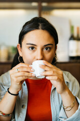 Portrait of a young latin woman drinking an expresso coffee in a bar