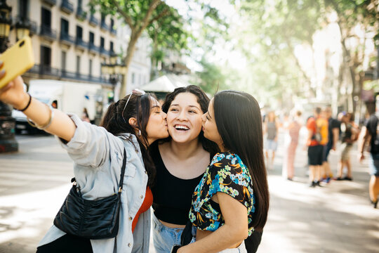 Three young women walking down Las Ramblas of Barcelona and taking a selfie, while kissing, with a phone