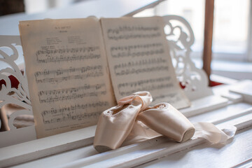 Fototapeta na wymiar Ballet pointe shoes on white grand piano with published notes.