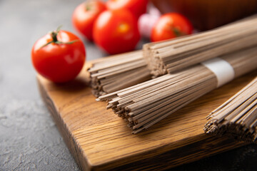 Buckwheat pasta with cherry tomatoes on a black textured marble background. Raw pasta. Ingredients for a gluten free dish. Healthy food. Place to copy.