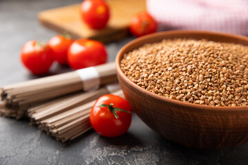 Buckwheat in a bowl with buckwheat paste and cherry tomatoes on a black textured marble background. Raw buckwheat. Ingredients for gluten free cereal. Healthy food. Place to copy.