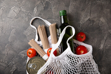 Ecobag with a grocery set. White string bag, shopper. Buckwheat sobo, cherry tomatoes, olive oil and canned meat. Shopping concept. Healthy food. Purchases.