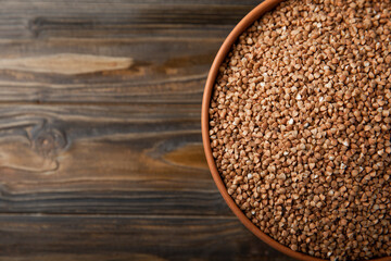 Buckwheat in a bowl on a brown textured wood background. Raw buckwheat. Ingredients for gluten free cereal. Healthy food. Place to copy.
