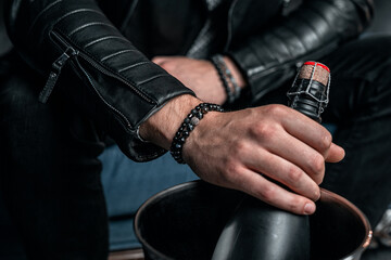Two stylish men's bracelets, on the wrist. Champagne bottle in hand, black background - obrazy, fototapety, plakaty