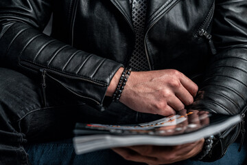 A black bracelet made of expensive stones on a man's hand, a leather jacket and a magazine