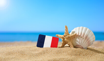 Fototapeta na wymiar Tropical beach with seashells and France flag. The concept of a paradise vacation on the beaches of France.
