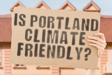 The question " Is Portland climate-friendly? " is on a banner in men's hands with blurred background. Support. Team. Activist. Urban. Sunset. Carbon. Ecology. Energy. New. Clean. Warming. Waste