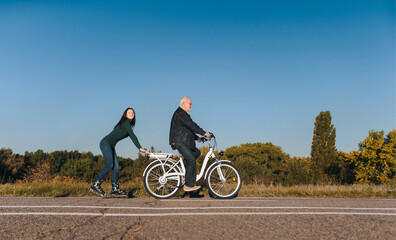 Obraz premium Young smiling caucasian girl on roller skates and a man on a electric bike fun ride together. Active leisure and hobbies. Father and daughter.