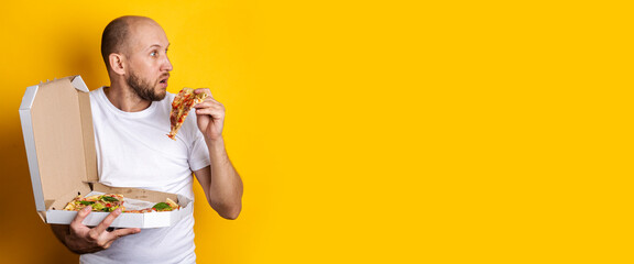 A young man took out a piece of pizza from the package, looking to the side in surprise on a yellow background. Banner