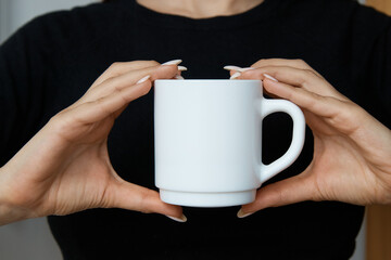 White mug for tea and coffee in the hands of a girl, close-up