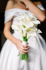 Beautiful wedding bouquet of white callas in hands of a young bride with a beautiful wedding manicure on nails.