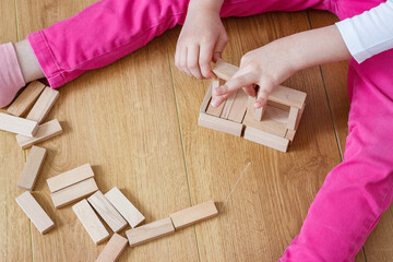 Little caucasian girl is playing wooden toys at home. Wooden blocks on wooden floor. Children's healthy game concept.