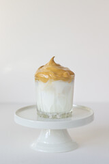 Distinctive layers of milk and whipped Dalgona coffee in a transparent mug, placed on a minimalist white background.